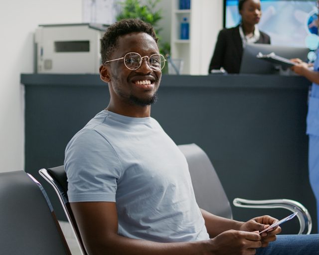 African american man waiting in hospital lobby, sitting in waiting room before attending checkup appointment with medic. Patient in facility reception having consultation with specialist.